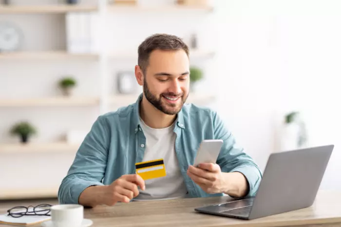 A person looking at a phone with a credit card in hand